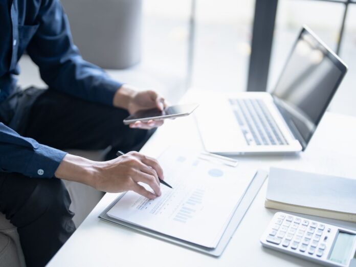 Pequeno empresário utilizando tecnologia e painéis digitais para organizar as finanças durante o cronograma da reforma tributária.